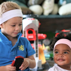 Puede incluir: Un niño con polo azul con emblema de león amarillo y diadema blanca, sosteniendo un coche de juguete rojo, junto a otro niño con diadema rosa claro y camiseta blanca, ambos en una zona de juegos.