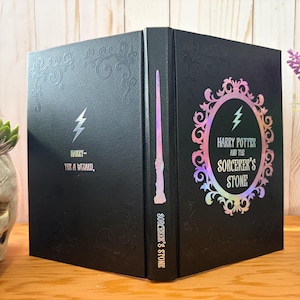 May include: Black book with embossed floral design and the text "Harry - Yes, a Wizard." The book features a lightning bolt and a holographic oval with the text "Harry Potter and the Sorcerer's Stone."
