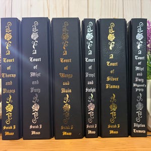 May include: A collection of six black hardcover books with gold, silver, and pink floral designs. The titles include "A Court of Thorns and Roses," "A Court of Mist and Fury," and "A Court of Wings and Ruin."