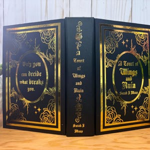 Puede incluir: Un libro negro con letras doradas y dise&ntilde;os florales. El t&iacute;tulo del libro es "A Court of Wings and Ruin" de Sarah J. Maas. La portada presenta la cita: "Solo t&uacute; puedes decidir qu&eacute; te rompe."