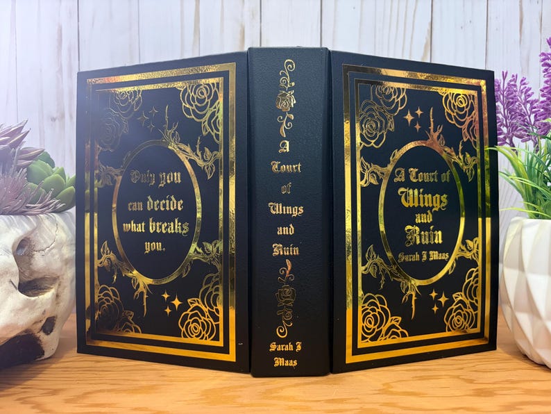 Puede incluir: Un libro negro con letras doradas y dise&ntilde;os florales. El t&iacute;tulo del libro es "A Court of Wings and Ruin" de Sarah J. Maas. La portada presenta la cita: "Solo t&uacute; puedes decidir qu&eacute; te rompe."