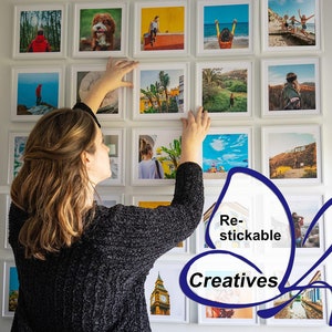 Op de afbeelding: Een vrouw hangt een galeriewand met ingelijste foto's op. De foto's zijn allemaal van verschillende grootte en tonen een verscheidenheid aan onderwerpen, waaronder landschappen, stadsgezichten en portretten. De foto's zijn allemaal afgedrukt op hoogwaardig papier en hebben een matte afwerking. De lijsten zijn allemaal wit en hebben een eenvoudig, modern ontwerp. De tekst "Re-stickable Creatives" is zichtbaar in de rechterbenedenhoek van de afbeelding.