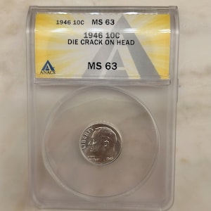 May include: A 1946 10-cent coin, graded MS 63, in a clear protective case. The case has text indicating a die crack on the coin's head. The coin shows the word "LIBERTY".