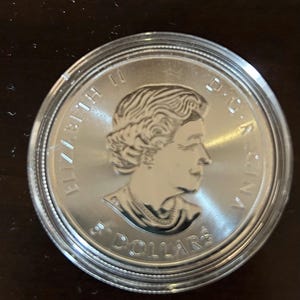 Könnte beinhalten: Eine silberne Münze mit einem Profilbild, in einer transparenten Kunststoffhülle. Die Münze trägt die Inschriften "ELIZABETH II D.G. REGINA" und "5 DOLLARS".