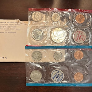 May include: A 1970 U.S. Mint Uncirculated Coin Set, packaged in clear plastic. The set includes various coins, such as quarters, dimes, and pennies. The packaging has red and blue accents. An envelope with text from the Treasury Department is also visible.