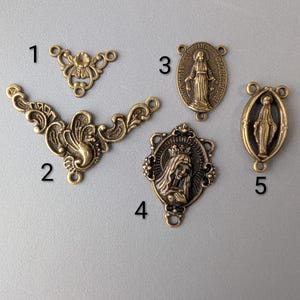 May include: An assortment of antique brass-toned metal charms and embellishments. The collection includes ornate filigree pieces and religious-themed pendants featuring images of the Virgin Mary. These components are ideal for jewelry making and craft projects.