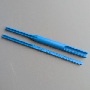 Peut inclure: Deux outils en plastique bleu clair. L'un a une longue poignée avec une fente et une extrémité fourchue. L'autre est similaire, avec le texte "OUR LADYS ROSARY MAKERS" imprimé dessus.