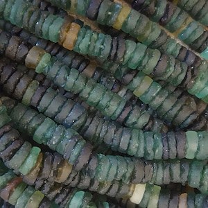 Pode incluir: Um close-up de um fio de contas de vidro verde, azul e marrom. As contas são feitas de vidro reciclado e têm uma superfície áspera e texturizada.