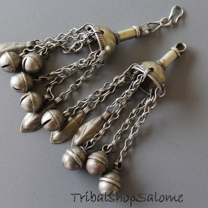 Peut inclure: Une paire de bijoux argentés avec des chaînes et des cloches pendantes. Chaque pièce a un dessus décoratif avec un crochet à l'extrémité.