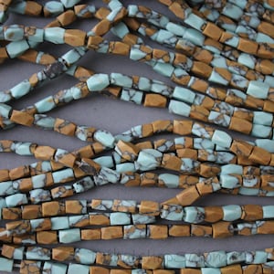 Peut inclure: Un brin de perles de turquoise et de pierre brune. Les perles sont facettées et de forme rectangulaire. Les perles sont enfilées sur un fil transparent.