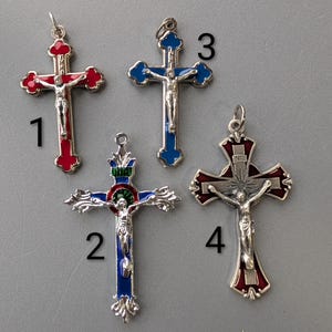 Puede incluir: Cuatro colgantes de cruz plateados con representaciones detalladas de Jesús. Las cruces presentan detalles de esmalte rojo y azul. Cada colgante tiene un lazo para sujetarlo a una cadena o collar.