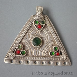 Peut inclure: Un pendentif triangulaire en argent avec des motifs complexes et des pierres précieuses vertes et rouges. Le pendentif a une boucle en haut pour l'attacher à une chaîne.