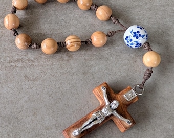 May include: A rosary featuring wooden beads and a decorative ceramic bead with blue floral patterns. The rosary includes a wooden crucifix with a silver figure of Jesus Christ.
