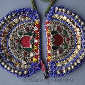 May include: A pair of silver and blue beaded jewelry pieces with red and green stones. The pieces are shaped like half-circles and are decorated with coins and bells.