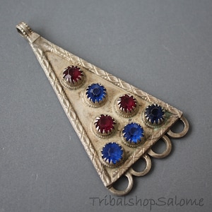 May include: A silver triangular pendant with red and blue glass stones set in a geometric pattern. The pendant has five loops at the bottom.
