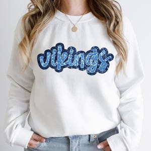 May include: White sweatshirt with a blue sparkly "Vikings" graphic.