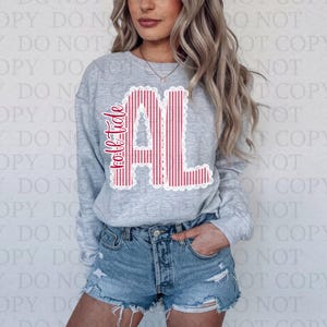 以下が含まれることがあります： 赤と白のストライプの「AL」の文字が白のスカラップデザインで縁取られた、明るい灰色のスウェットシャツ。「Roll Tide」の文字が文字の左側に赤で縦書きされています。