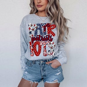 Pode incluir: Uma camisola cinza claro com a palavra "Patriots" em vermelho, branco e azul, com padrões de estrelas e bolinhas. A camisola é combinada com calções de ganga.