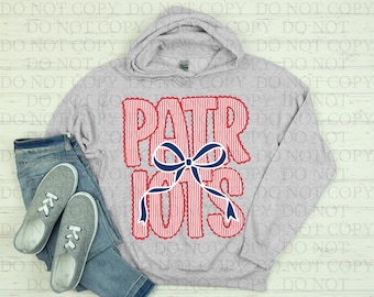 May include: A light gray hooded sweatshirt with the word "PATRIOTS" in red and white striped letters, and a blue bow. The sweatshirt is paired with blue jeans and gray sneakers.