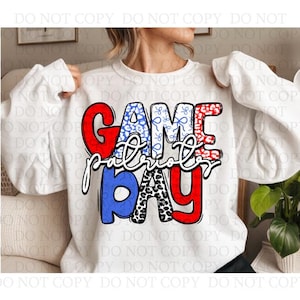 Könnte beinhalten: Weißes Sweatshirt mit dem Schriftzug "GAME DAY Patriots" in Rot, Blau und Schwarz. Die Buchstaben sind mit Mustern wie Leopardenmuster und einem blau-weißen Design verziert. Das Sweatshirt wird getragen.