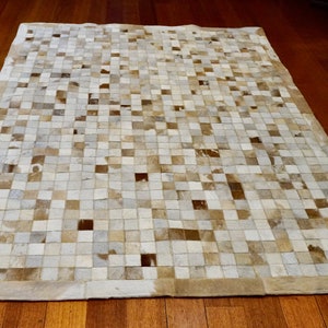 May include: A white and brown patchwork cowhide rug with a square pattern. The rug has a white border.