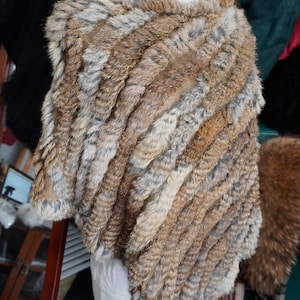 Puede incluir: Un poncho de piel sintética marrón y gris con un patrón a rayas. El poncho está drapeado sobre un maniquí blanco.