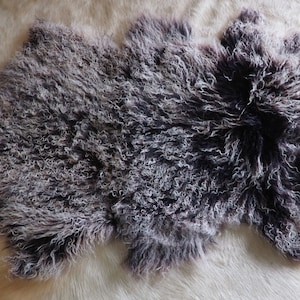 Puede incluir: Una alfombra de piel de oveja esponjosa con un patrón de color gris oscuro y blanco. La alfombra es suave y mullida, y sería perfecta para agregar un toque de calidez y comodidad a cualquier habitación.