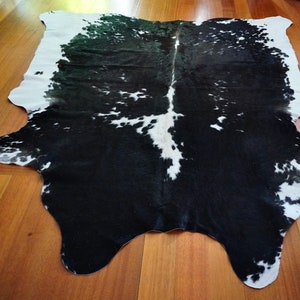 Puede incluir: Alfombra de piel de vaca negra y blanca con una forma natural irregular. La piel es principalmente negra con manchas blancas.