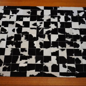 May include: Black and white cowhide rug with a checkered pattern. The rug is made of individual pieces of cowhide sewn together.
