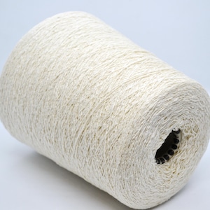 Puede incluir: Un cono grande de hilo blanco roto. El hilo está enrollado firmemente, mostrando una superficie texturizada. El cono tiene forma cilíndrica con un centro hueco. El hilo parece ser una fibra natural, adecuado para proyectos de tejido o ganchillo.