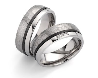 May include: Two silver wedding bands with a textured finish. One band has a black inlay and the other has three small diamonds.