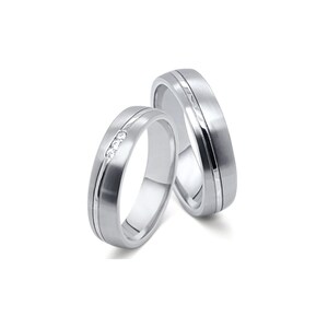 Puede incluir: Dos anillos de boda plateados. Uno presenta tres pequeños diamantes, mientras que el otro tiene una superficie texturizada y un borde pulido. Ambos anillos tienen un diseño simple y elegante, perfecto para una boda o compromiso.
