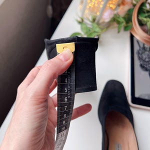 May include: Black suede shoe with a square toe. A measuring tape shows the heel height is approximately 7.6 cm. The shoe is on a white surface.