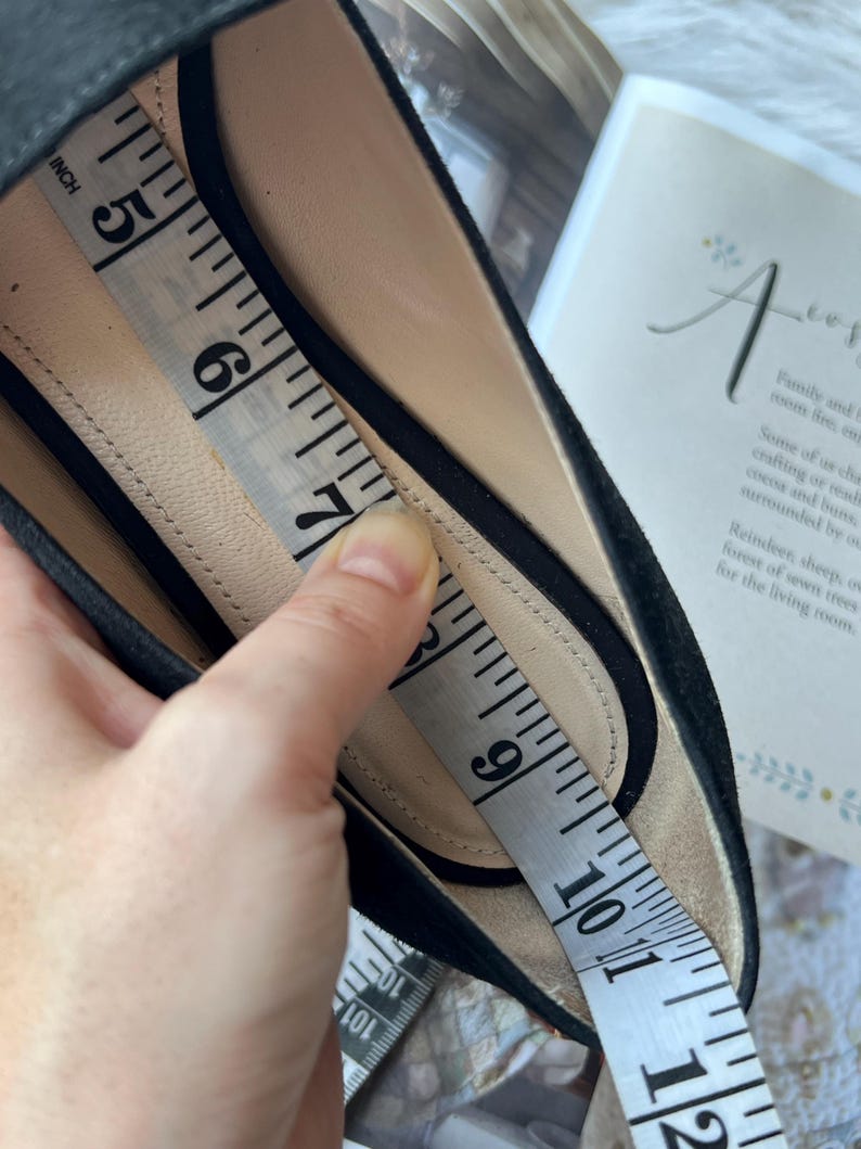 K&ouml;nnte beinhalten: Ein schwarzer Schuh mit beigem Innenfutter. Ein wei&szlig;es Ma&szlig;band liegt im Schuh und zeigt eine L&auml;ngenmessung von etwa 12,7 cm bis 25,4 cm entlang der Innensohle des Schuhwerks an.