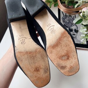 May include: A pair of black suede heeled shoes, size 39, with square toes and block heels. The soles show wear and the heels have a textured rubber base. The shoes are likely vintage or pre-owned.