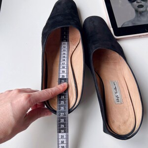 May include: Black suede slip-on shoes with a pointed toe. A measuring tape shows the shoe's length. The shoes have a leather insole with the brand name "Stefi Talman". The shoes are approximately 30 cm long.