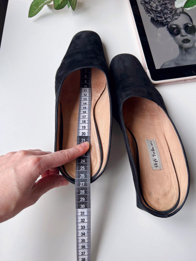 May include: Black suede slip-on shoes with a pointed toe. A measuring tape shows the shoe's length. The shoes have a leather insole with the brand name "Stefi Talman". The shoes are approximately 30 cm long.