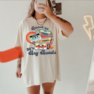 May include: A white t-shirt with a graphic design of cassette tapes and the text "Raised on 90's Boy Bands".