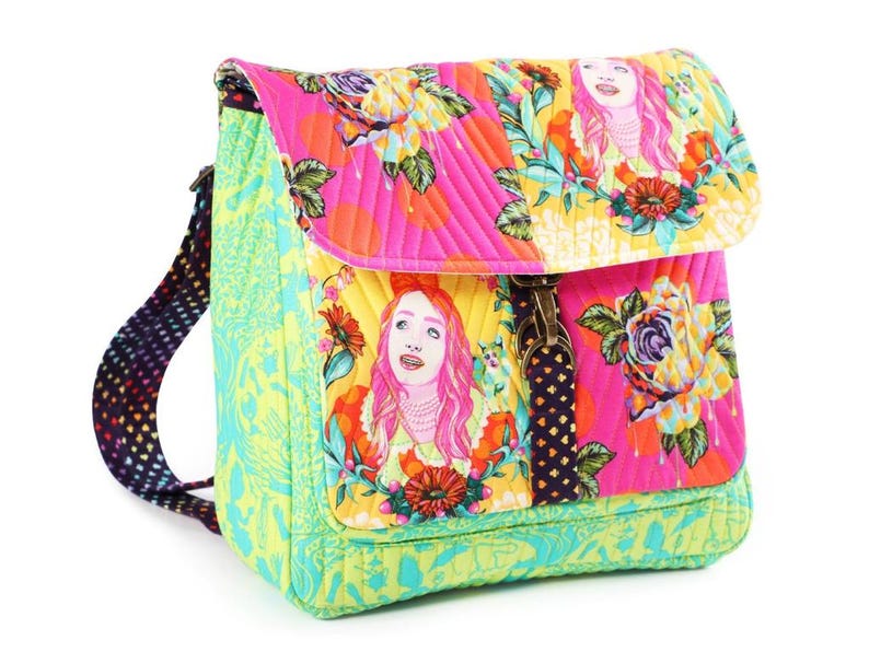 Puede incluir: Una mochila de tela acolchada con un vibrante estampado floral multicolor e ilustraciones de una persona con cabello rosa. La bolsa incluye un panel lateral verde lima, una correa oscura con un patr&oacute;n peque&ntilde;o y un cierre de metal en el frente.