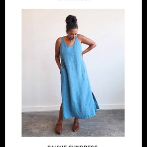 May include: A blue sleeveless sundress with a V-neckline and side slits. The dress is shown on a model with brown shoes. The text "SAUVIE SUNDRESS" is at the bottom of the image, along with the text "STANDARD SIZES 00 - 20" and "CONFIDENT BEGINNER".