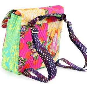 Puede incluir: Una mochila acolchada con un dise&ntilde;o de patchwork vibrante en paneles de color rosa brillante, amarillo y verde lima. El bolso muestra patrones florales y una ilustraci&oacute;n de retrato, complementada con correas ajustables moradas con corazones.