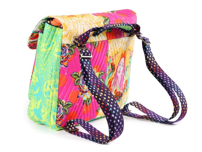 Puede incluir: Una mochila acolchada con un dise&ntilde;o de patchwork vibrante en paneles de color rosa brillante, amarillo y verde lima. El bolso muestra patrones florales y una ilustraci&oacute;n de retrato, complementada con correas ajustables moradas con corazones.