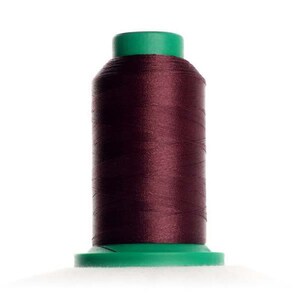 May include: A spool of dark maroon thread with a green plastic top and bottom.