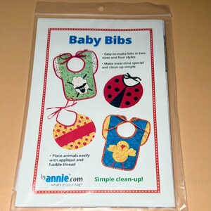 May include: A package containing a pattern for baby bibs. The pattern features four bib designs with animal appliqués, including a sheep, ladybug, and chick. Text on the package reads "Baby Bibs" and "Simple clean-up!"