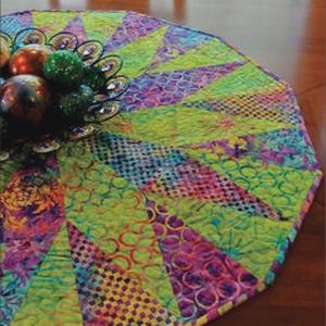 May include: A colorful, quilted table topper with a vibrant design. The topper features a mix of green, purple, and yellow fabrics arranged in a fan-like pattern. Text on the image reads "Over Under" and "Swirly Girls".