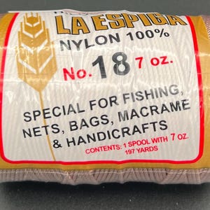 May include: A spool of beige nylon thread, labeled "LA ESPIGA," with the text "NYLON 100%" and "No. 18 7 oz." The label indicates it's for fishing, nets, bags, macrame, and handicrafts. The spool contains 7 oz. of thread.