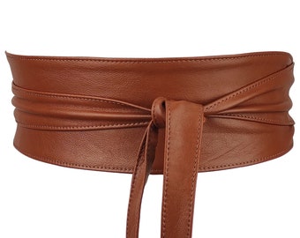 Op de afbeelding: Een bruine leren riem met een lange stropdas die om de taille gewikkeld kan worden en in een strik geknoopt kan worden. De riem is gemaakt van zacht, soepel leer en heeft een eenvoudig, elegant ontwerp.
