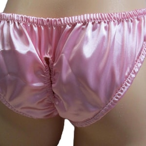 May include: A pair of light pink satin underwear featuring a shiny, smooth finish with an elasticized waistband and leg openings. The garment includes a vertical gathered seam detail along the center back, creating a ruched effect in the fabric.