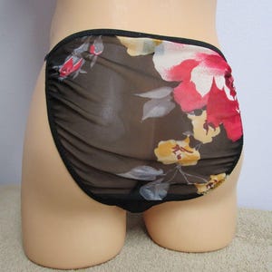 May include: High-cut underwear made of a sheer, dark brown mesh fabric featuring a vibrant floral print with large red and yellow flowers and green leaves. The garment is finished with a solid black elastic trim along the waist and leg openings.