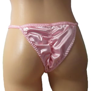 May include: A pair of light pink satin thong underwear featuring a gathered center seam detail along the back. The garment is constructed with thin, matching pink fabric straps at the waist and finished with a delicate, textured trim along the edges.